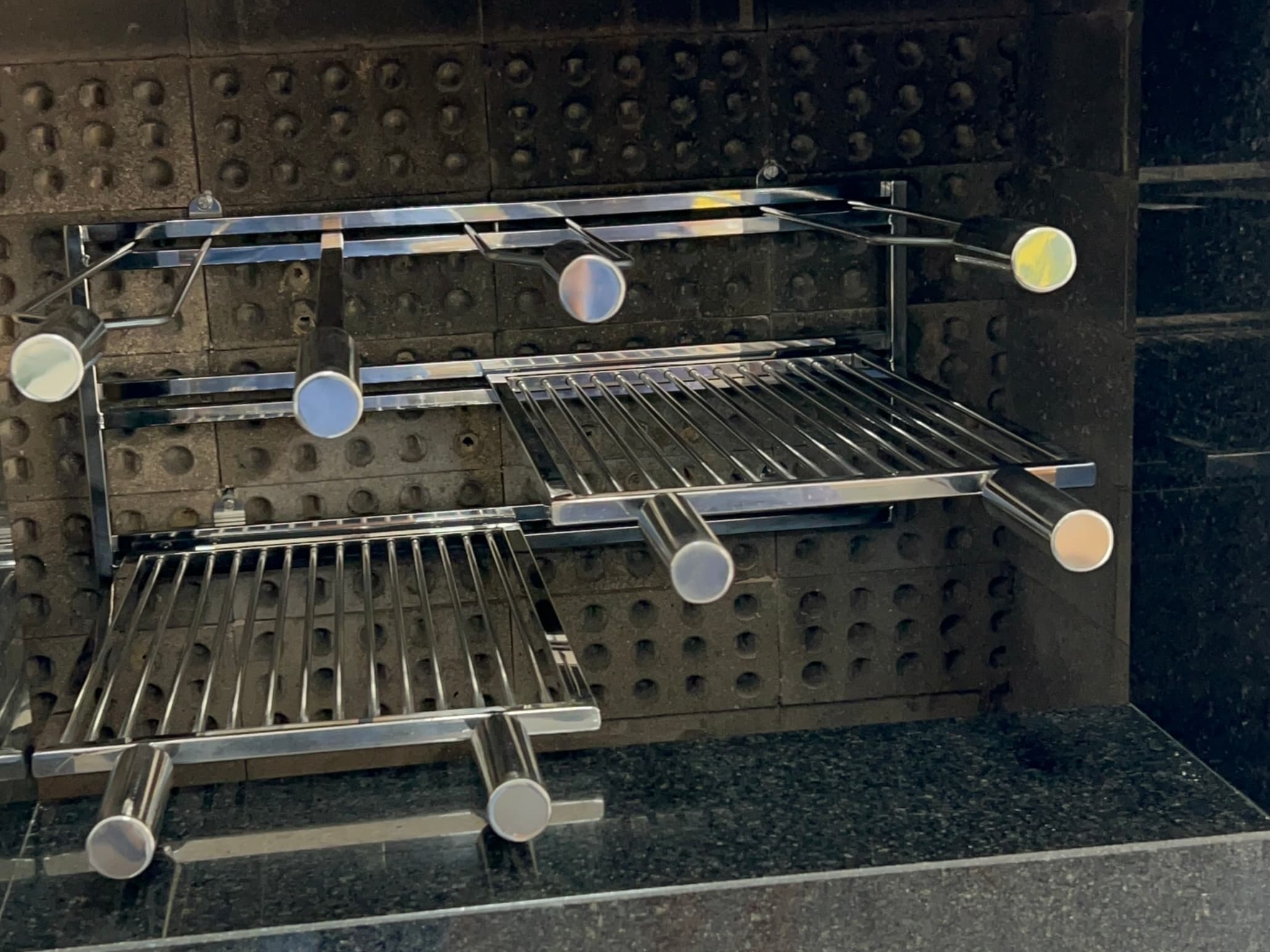 Espetos e grelhas de inox encaixados juntos no suporte aéreo, em alturas diferentes