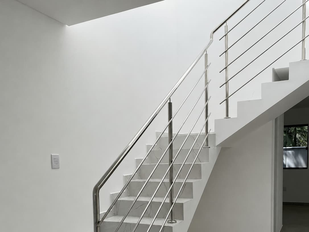 Guarda-corpo de inox com tubos horizontais ao longo de escada de mármore branco, em ambiente de pé-direito duplo